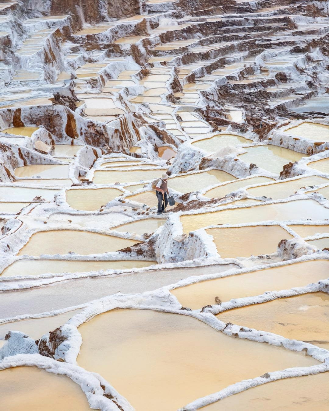 Detailed view of the Maras Salt Mines in Cusco, Peru, featuring glistening salt pools and a person walking among the terraces.