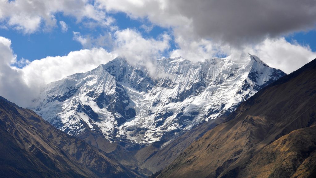 Snow-covered mountain peaks surrounded by rugged terrain and a partially cloudy blue