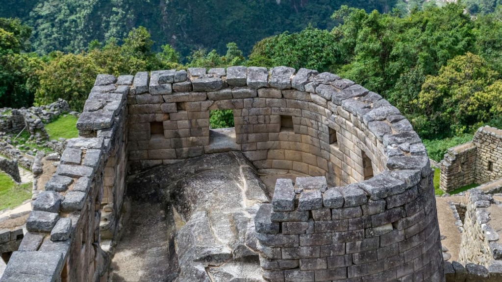 Templo del Sol en Machu Picchu con su estructura semicircular de piedra, construido sobre una roca sagrada y rodeado de vegetación. -Xplora Machu Picchu