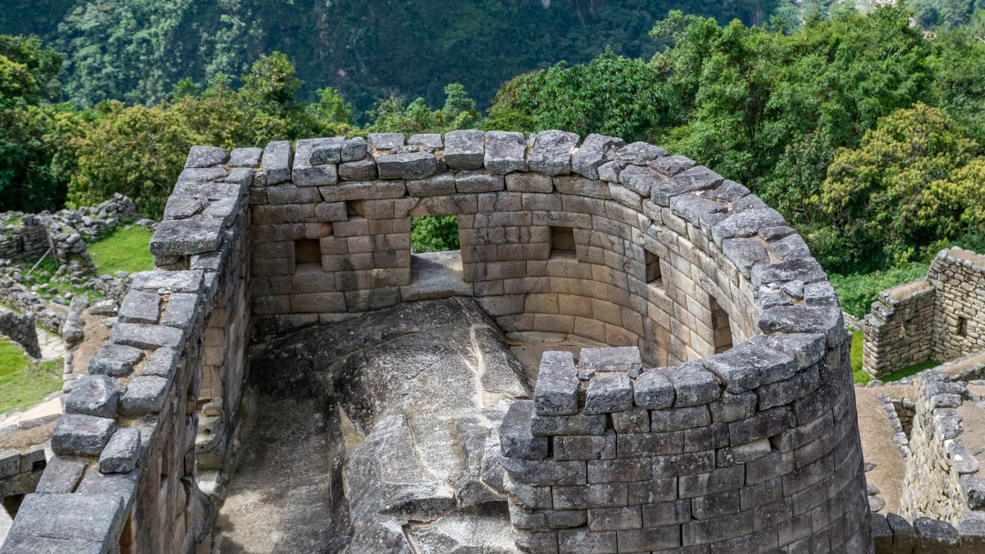 Templo del Sol en Machu Picchu con su estructura semicircular de piedra, construido sobre una roca sagrada y rodeado de vegetación. -Xplora Machu Picchu