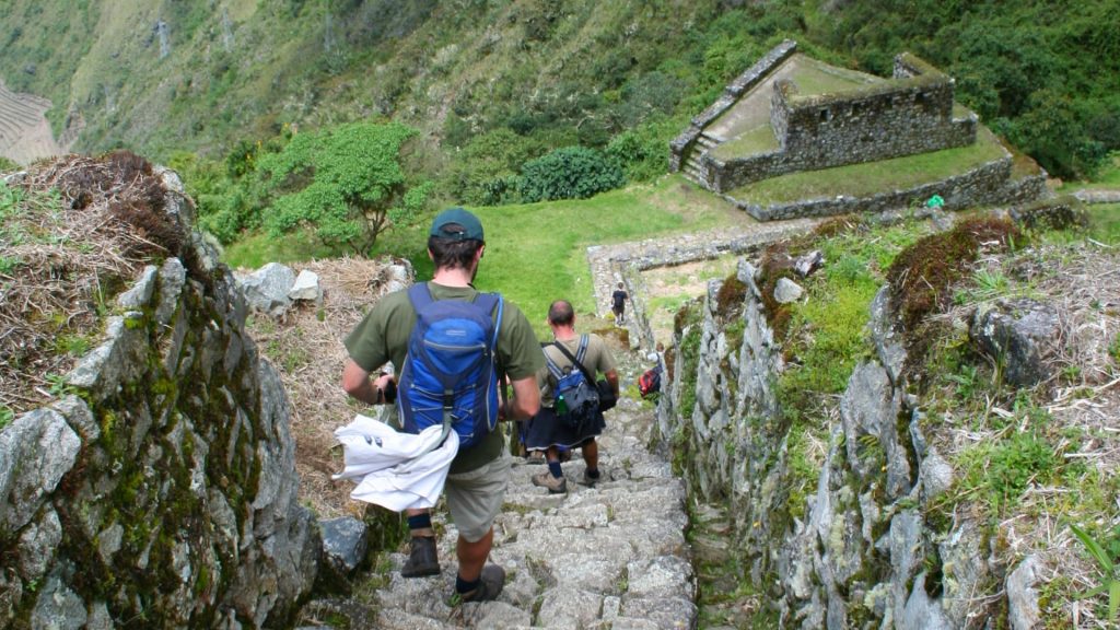 Hikers descending ancient Inca stone steps surrounded by lush greenery and stone ruins on the Inca Trail to Machu Picchu.