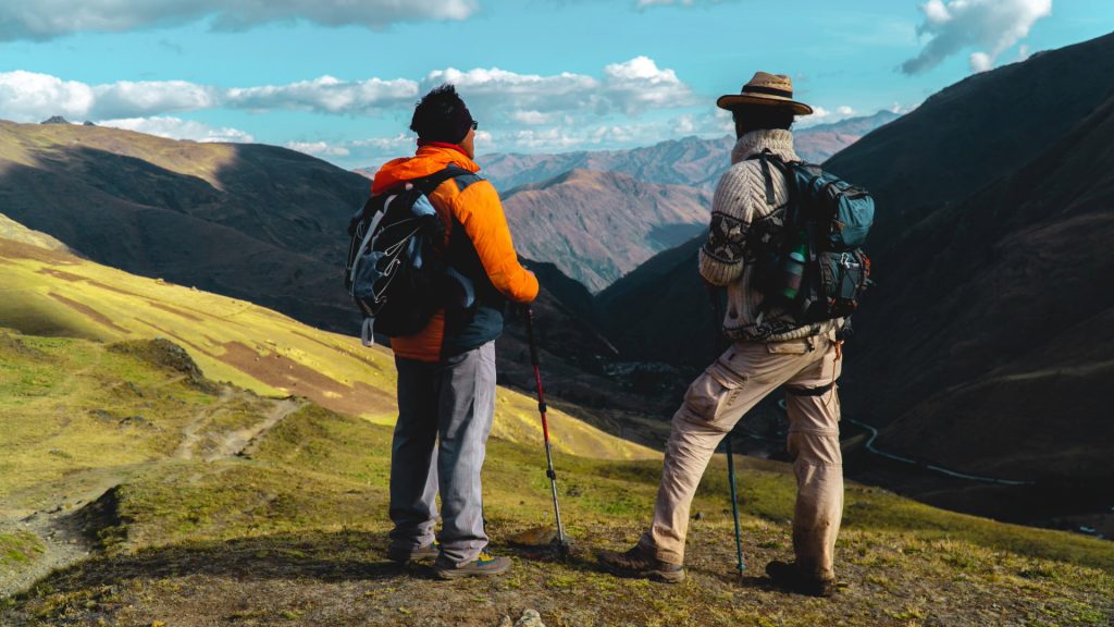 Two hikers standing on a mountain ridge along the Lares Trek, admiring the breathtaking Andean valley views.