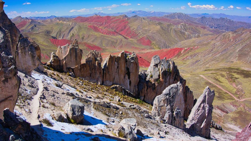 Jagged rock formations with a scenic backdrop of red and green mountains under a bright blue sky - Xplor Machupicchu
