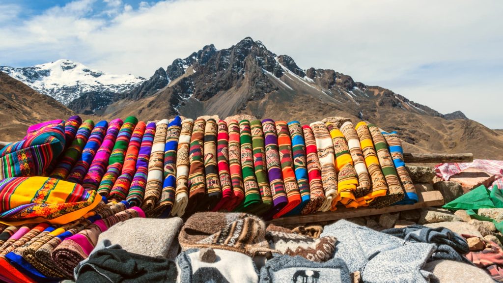 Colorful Andean handwoven textiles displayed against a stunning mountain backdrop, showcasing traditional craftsmanship - Xplor Machu Picchu.