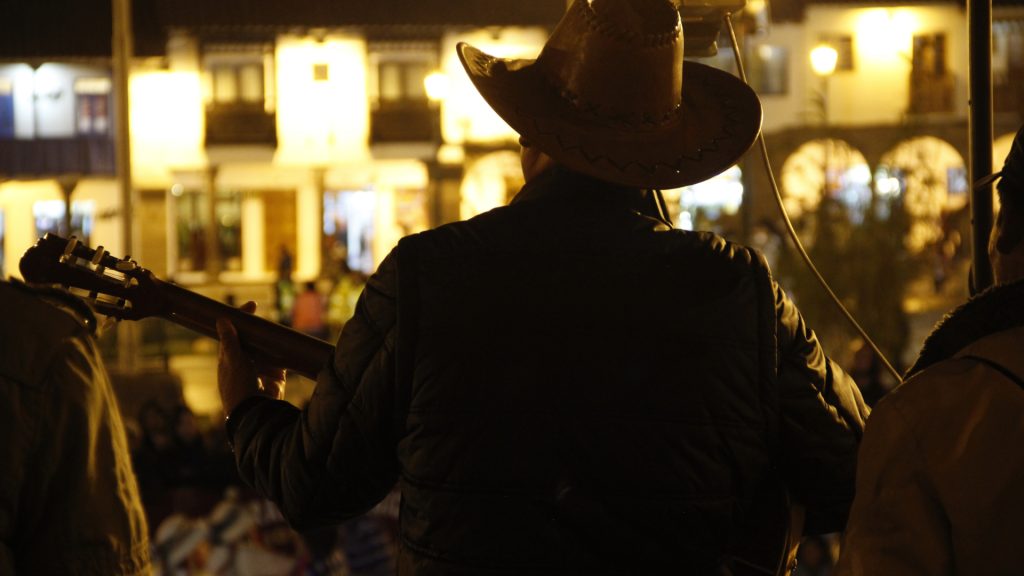 Performer with a hat playing traditional music during Cusco’s nightlife, capturing the artistic atmosphere of the city’s nocturnal streets - Xplor Machupicchu