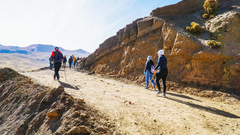 A group of hikers trekking along a rugged mountain trail in the Andes, surrounded by rocky cliffs and breathtaking high-altitude scenery Cusipata- Xplor MachuPicchu