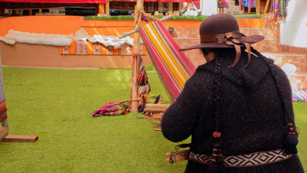 Mujer andina tejiendo en un telar tradicional con colores vibrantes, preservando las técnicas ancestrales del textil en los Andes - Xplor Machu Picchu.
