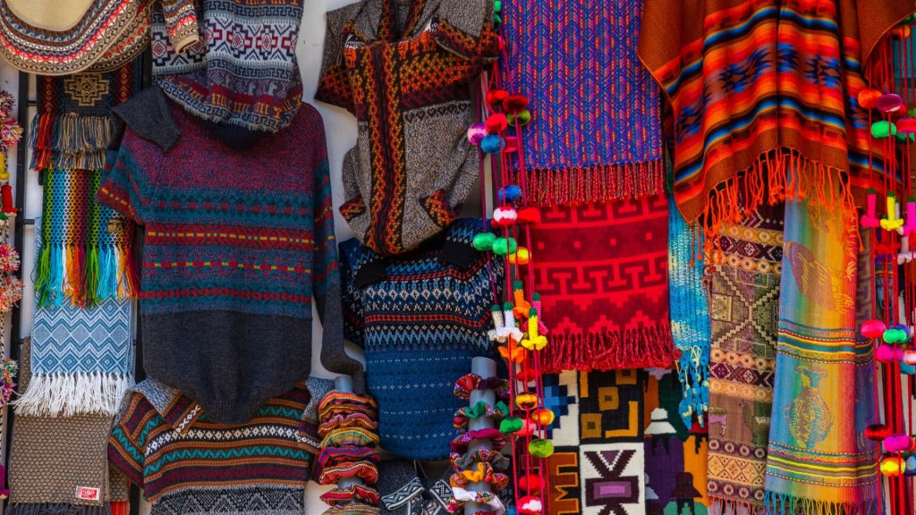 Colorful ponchos, sweaters, and blankets displayed in a traditional Cusco artisan market - Xplor Machu Picchu