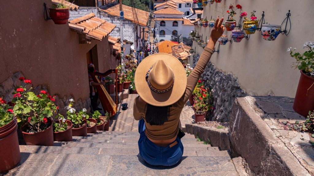 Woman sitting on flower-decorated stairs in San Blas, one of Cusco’s most charming neighborhoods - Xplor Machu Picchu