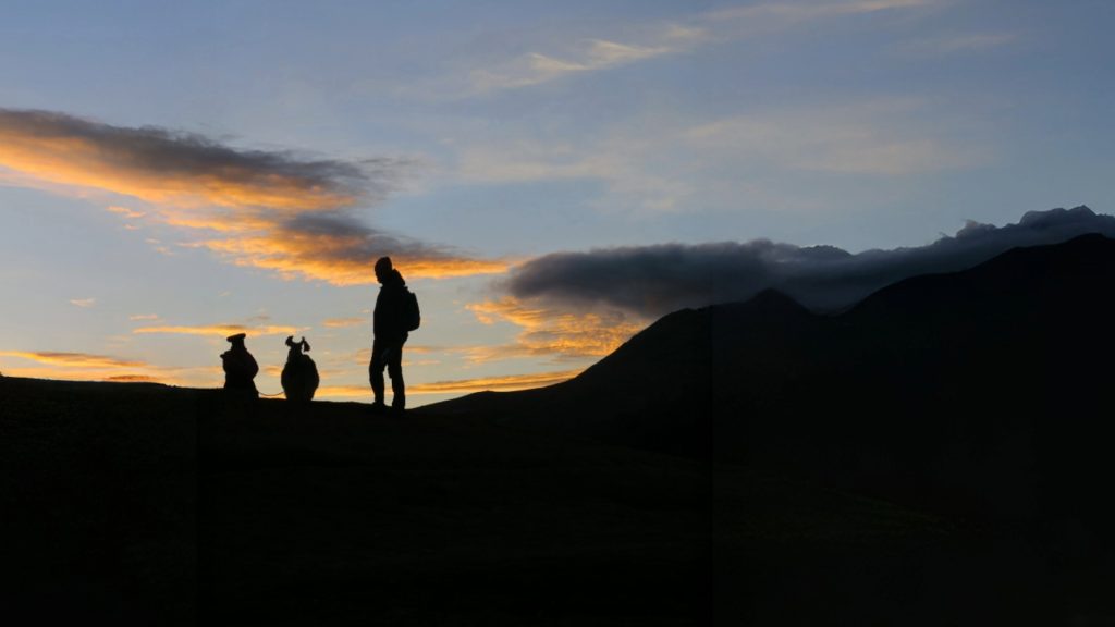 Three people watching the sunset in the sacred mountains, surrounded by the Apus of Cusco - Xplor Machu Picchu