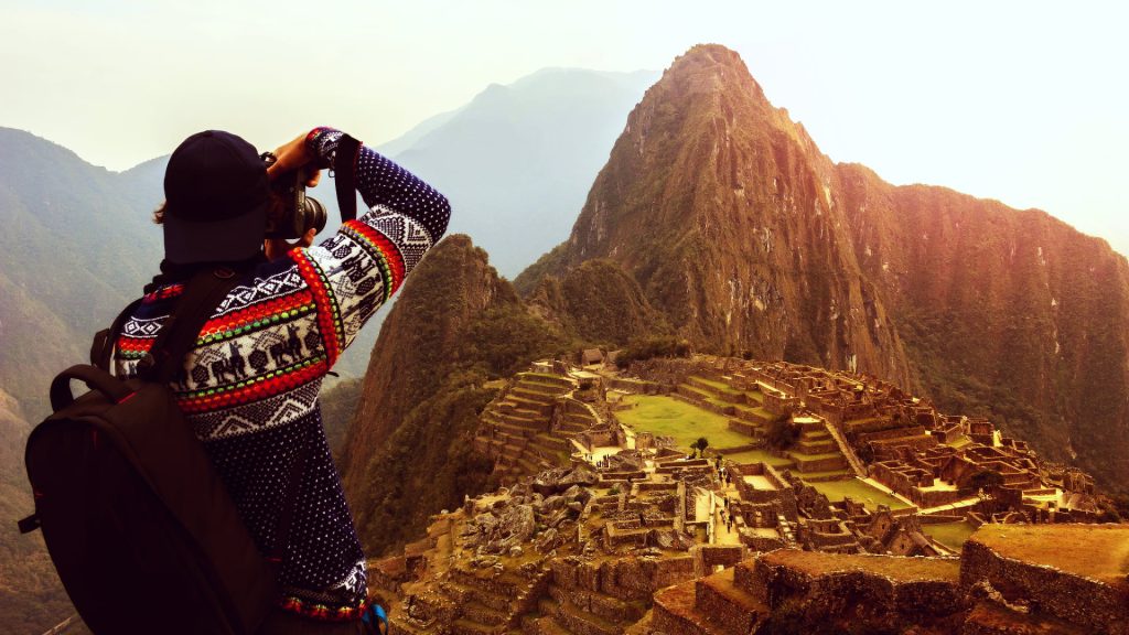 Tourist capturing Machu Picchu at golden hour, a key example for Photography Tips Machu Picchu - Xplor Machu Picchu